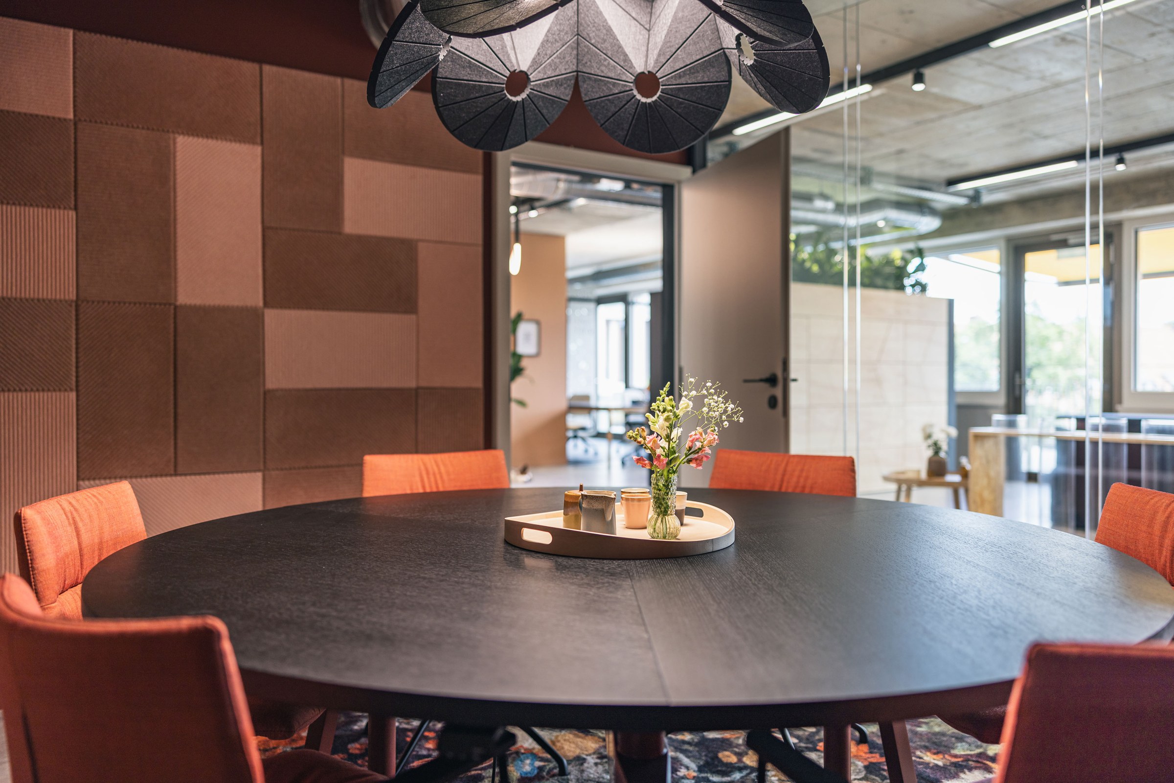 Eleganter Meetingraum mit rundem schwarzem Tisch, dekorativer Wandverkleidung und Blumenarrangement.