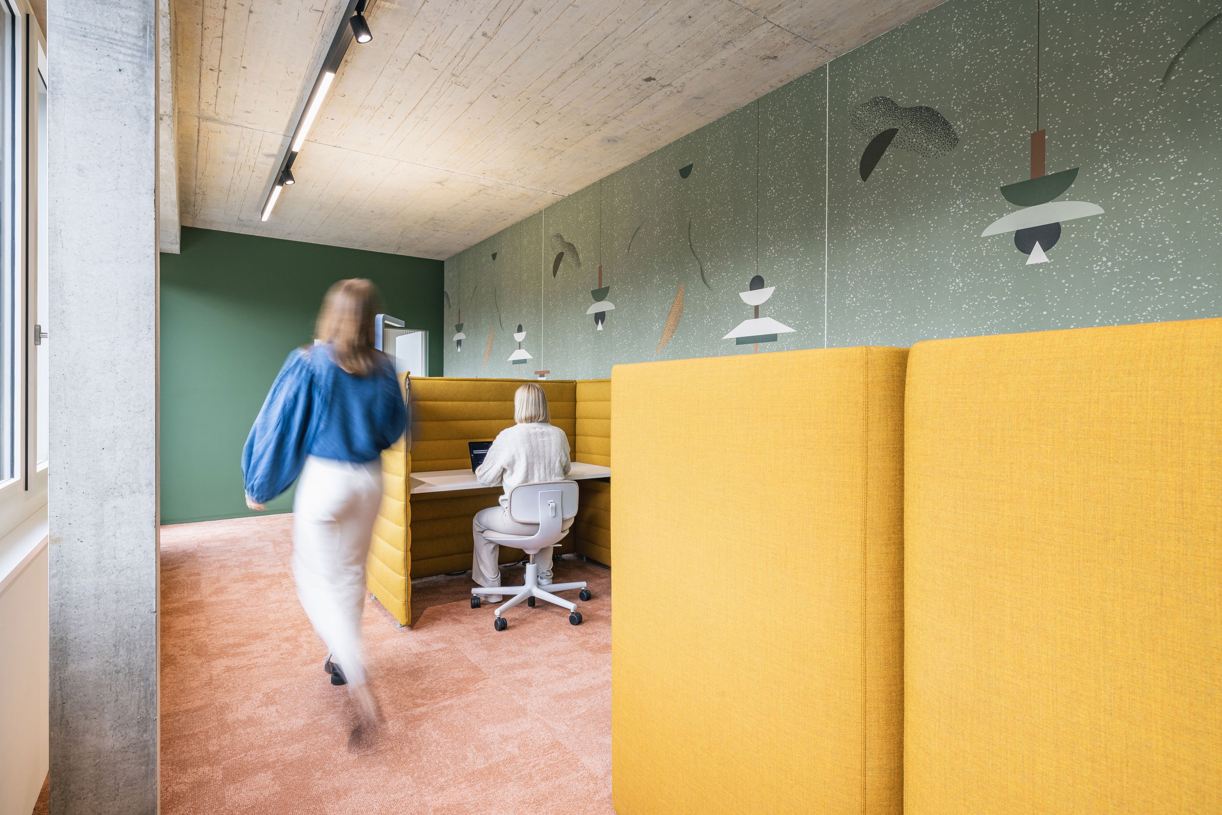 Ruhige Fokuszone mit gelben Akustik-Workpods, grün gestalteter Wand und warmem Teppichboden.