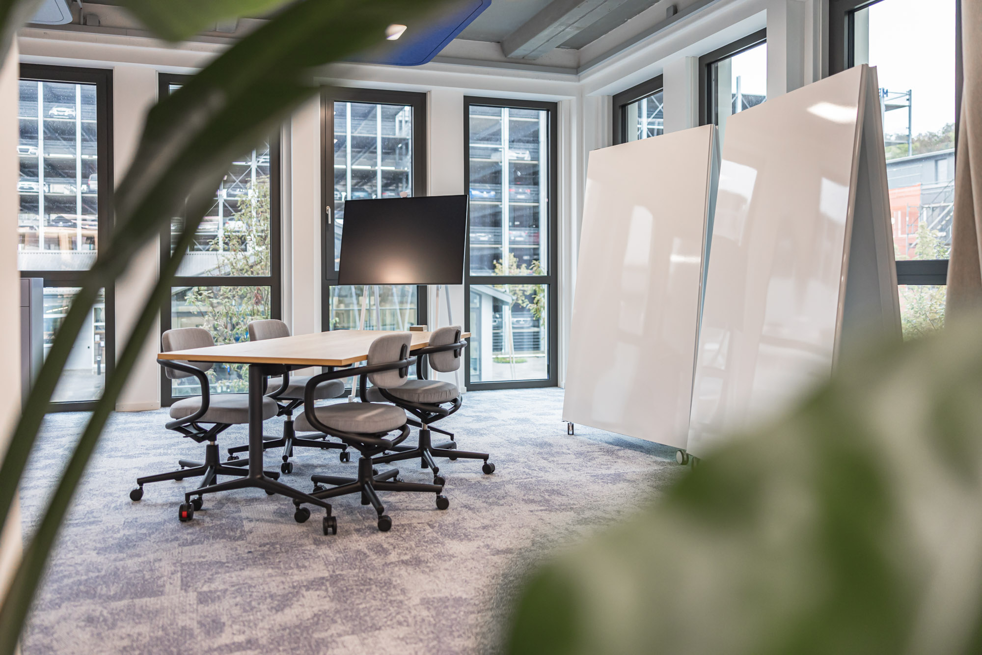 Heller Kreativraum mit mobilen Whiteboards, großem Tisch und flexiblen Drehstühlen. Viel Tageslicht, klare Linien.