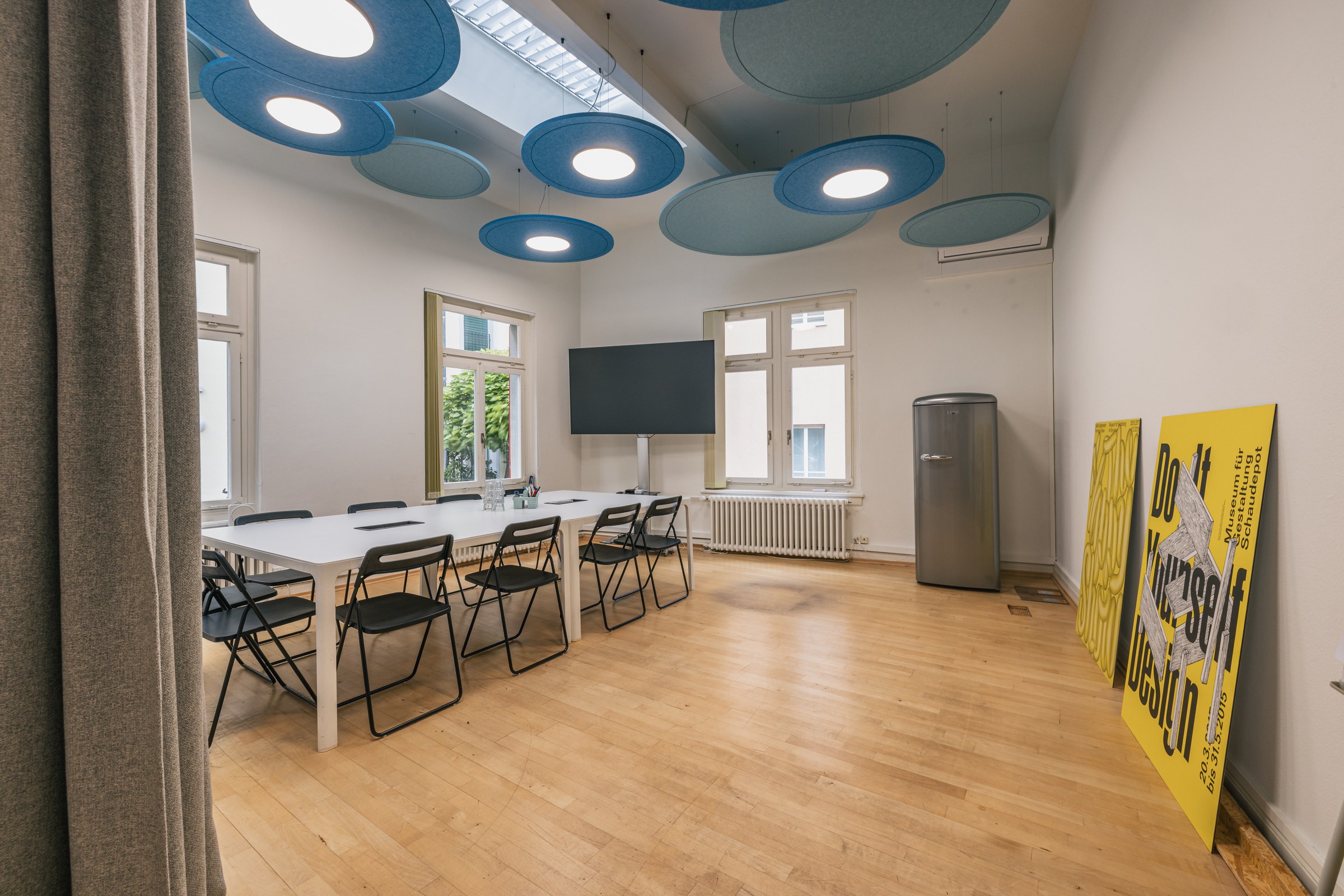 Heller Meetingraum mit großen blauen Akustikdeckenpaneelen, langem Tisch und schwarzem Monitor.