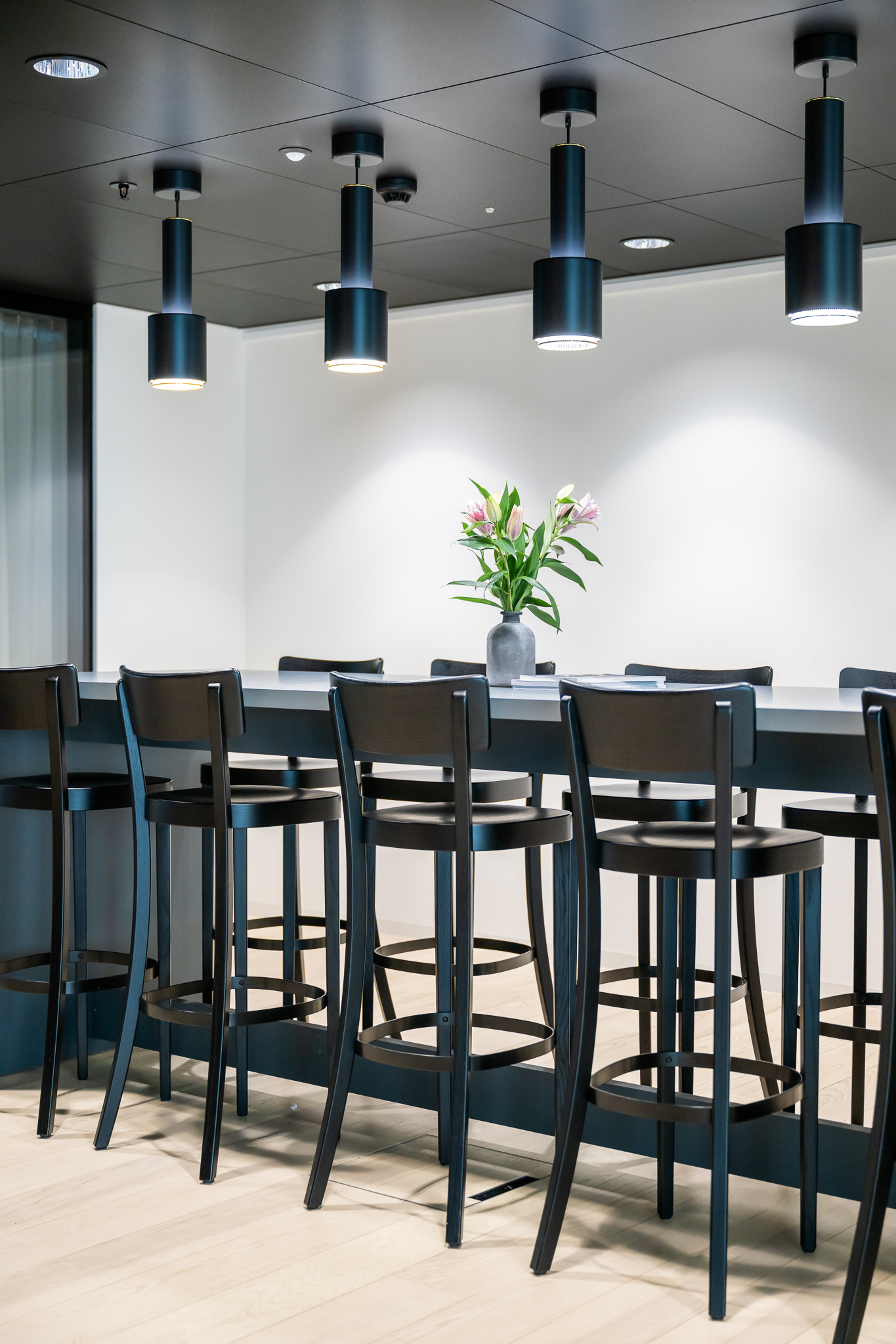 Eleganter Meetingbereich mit hohem Tisch, schwarzen Barstühlen und modernen Pendelleuchten unter dunkler Decke.