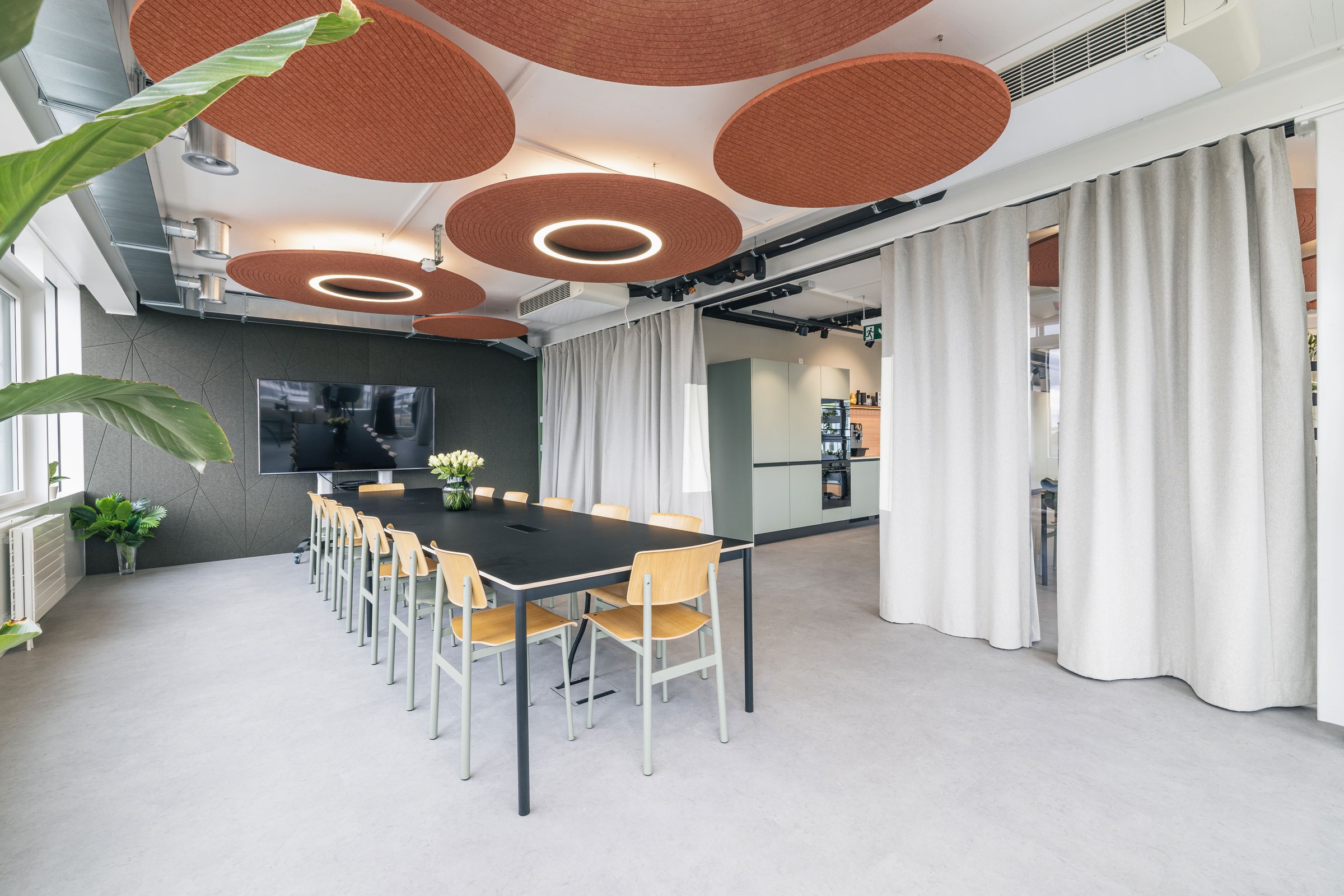 Offener Workshopraum mit langem Besprechungstisch, Akustikdecken und großem Bildschirm.