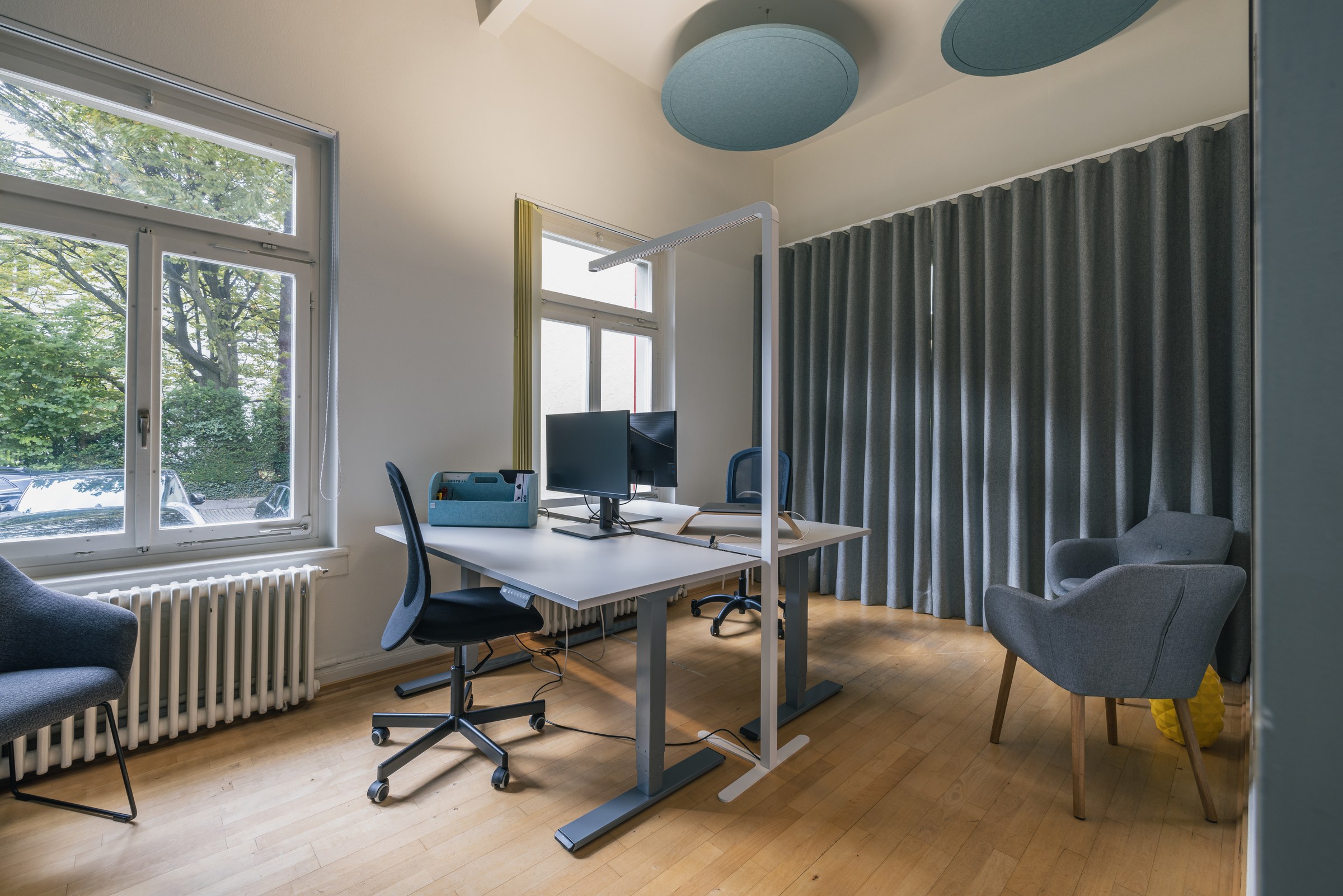 Zweigeteilter Workspace mit höhenverstellbaren Schreibtischen, Akustikvorhängen und großen Fenstern.