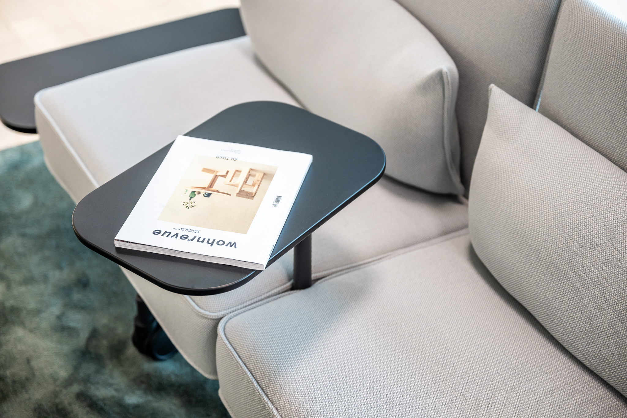 Detailaufnahme eines hellgrauen Sofas mit integriertem Ablagetisch und aufgelegtem Wohnen-Magazin.