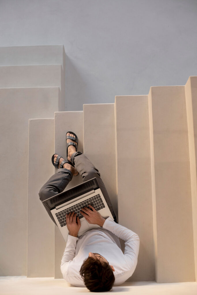 Mann mit Laptop auf Treppe sitzend.