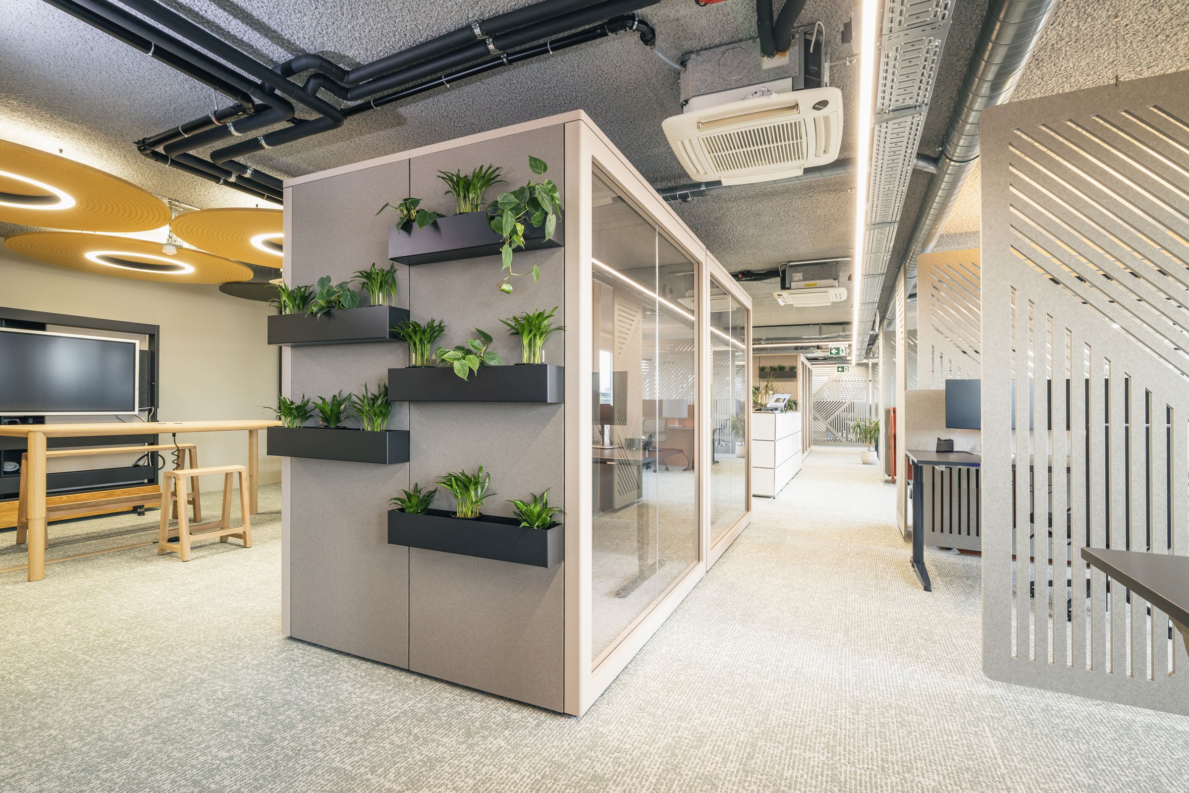 Innovativer Büroarbeitsbereich mit gläserner Meetingbox und vertikalem Pflanzensystem.