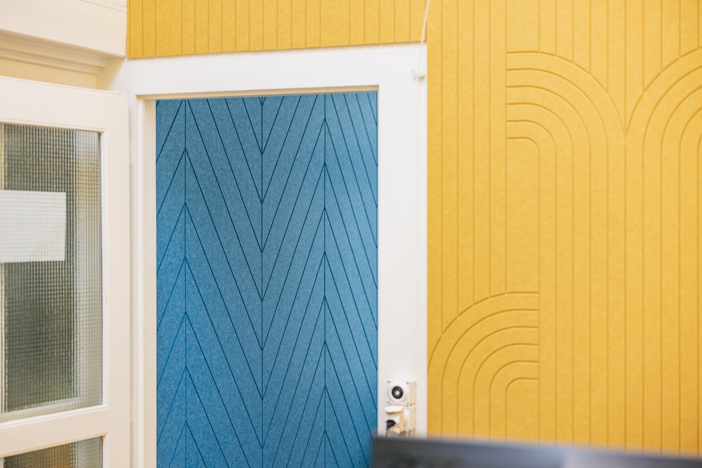 Detailaufnahme farbiger Akustikpaneele in Blau und Gelb mit grafischen Linienmustern.