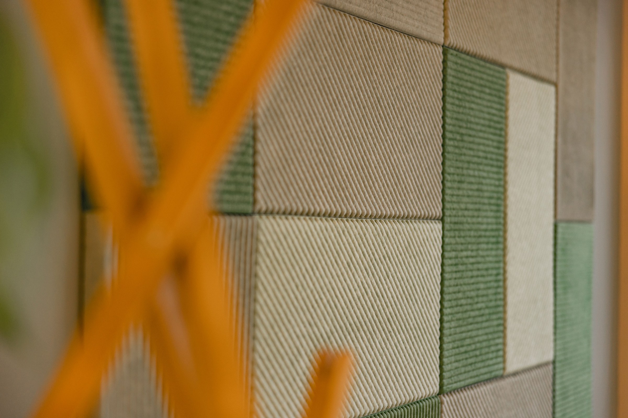 Detailaufnahme grüner und beige strukturierter Akustikpaneele an einer Wand.