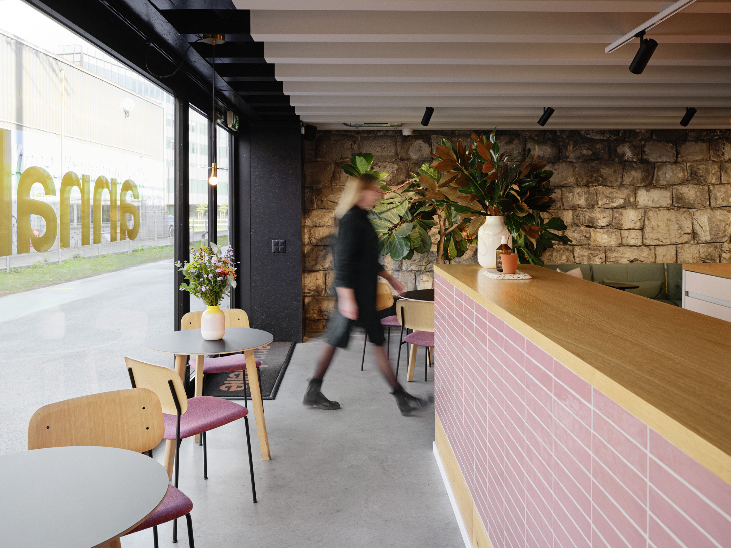 Nahaufnahme eine Theke mit pinken Kacheln. Daneben Coffee-Table mit Stühlen. Eine Person läuft vorbei.