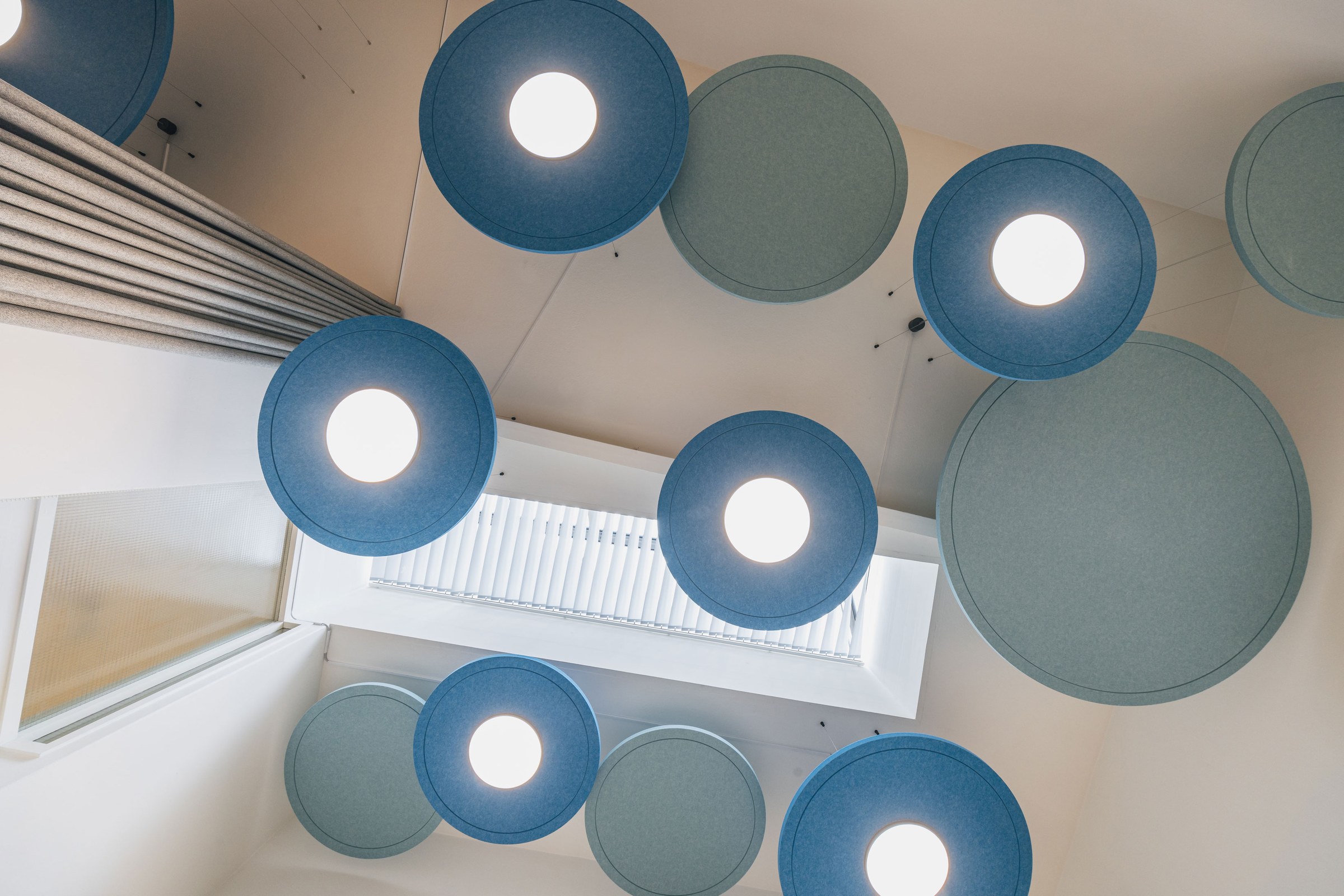 Runde blaue Akustikpaneele mit integrierter Beleuchtung, von unten durch ein Oberlicht fotografiert.