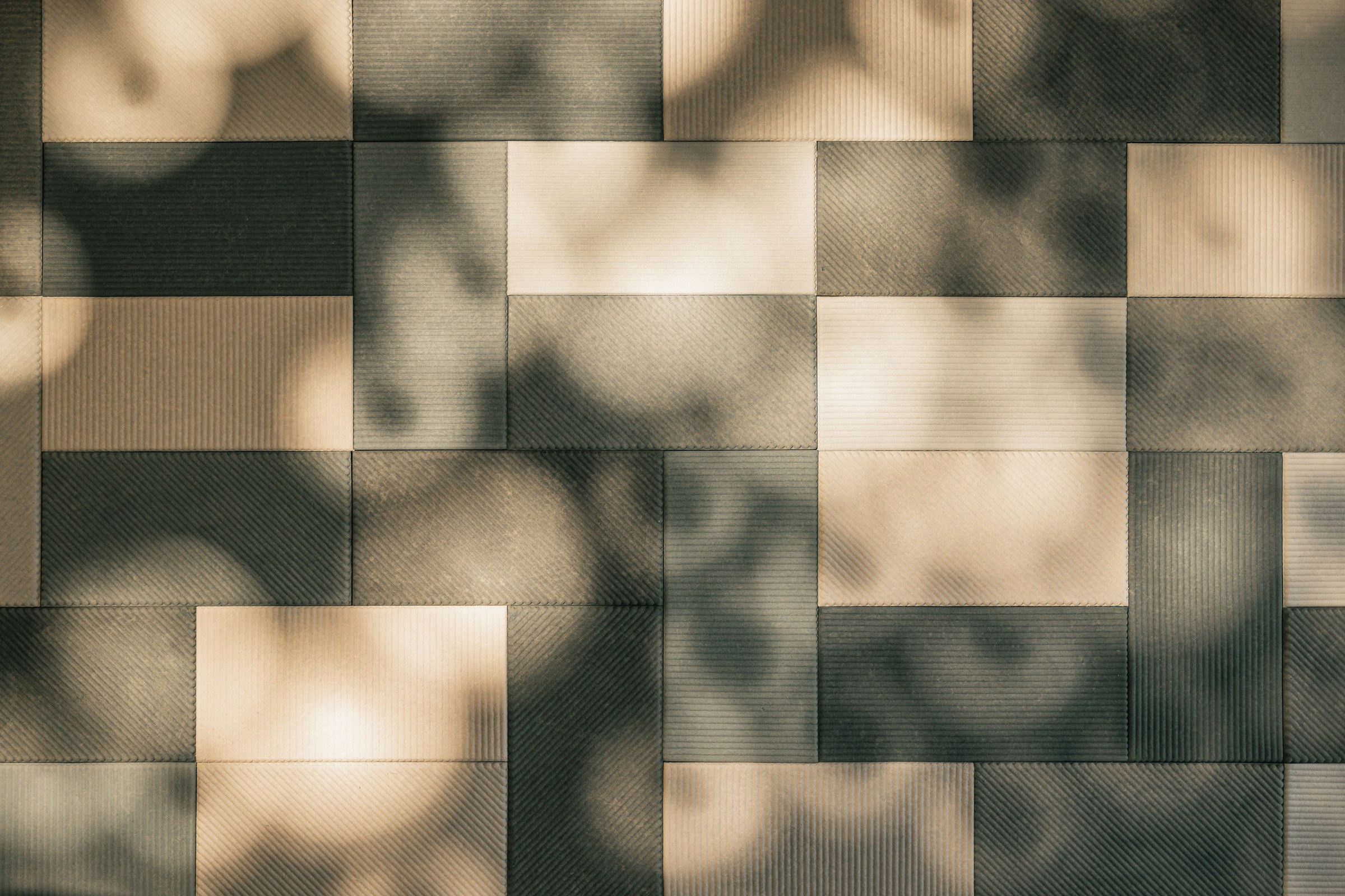 Detailaufnahme einer geometrisch angeordneten Wandverkleidung aus rechteckigen, strukturierten Paneelen in Naturtönen.