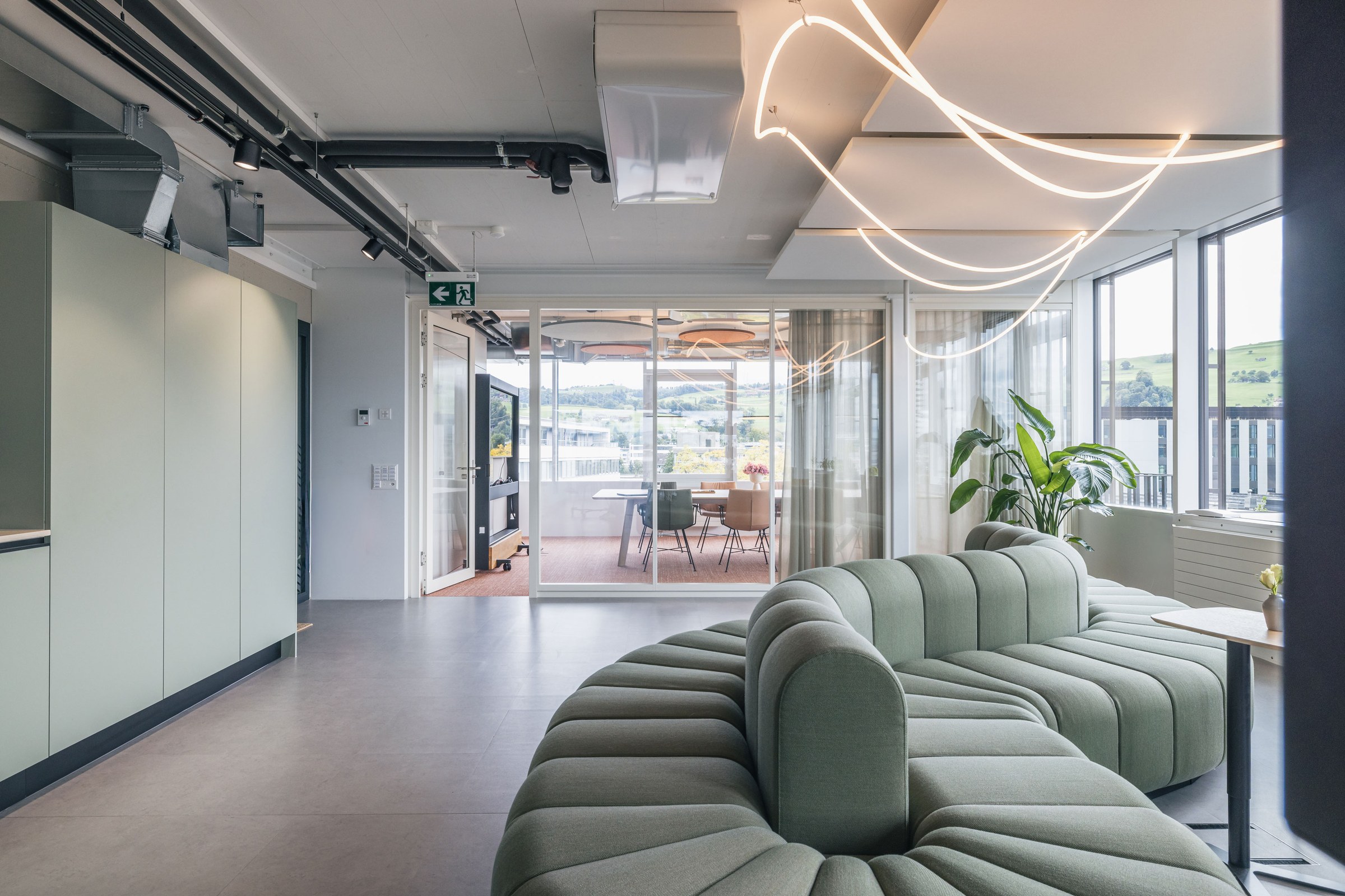 Großer Büro-Loungebereich mit geschwungenem Sofadesign und Panoramafenstern mit Blick auf die Umgebung.