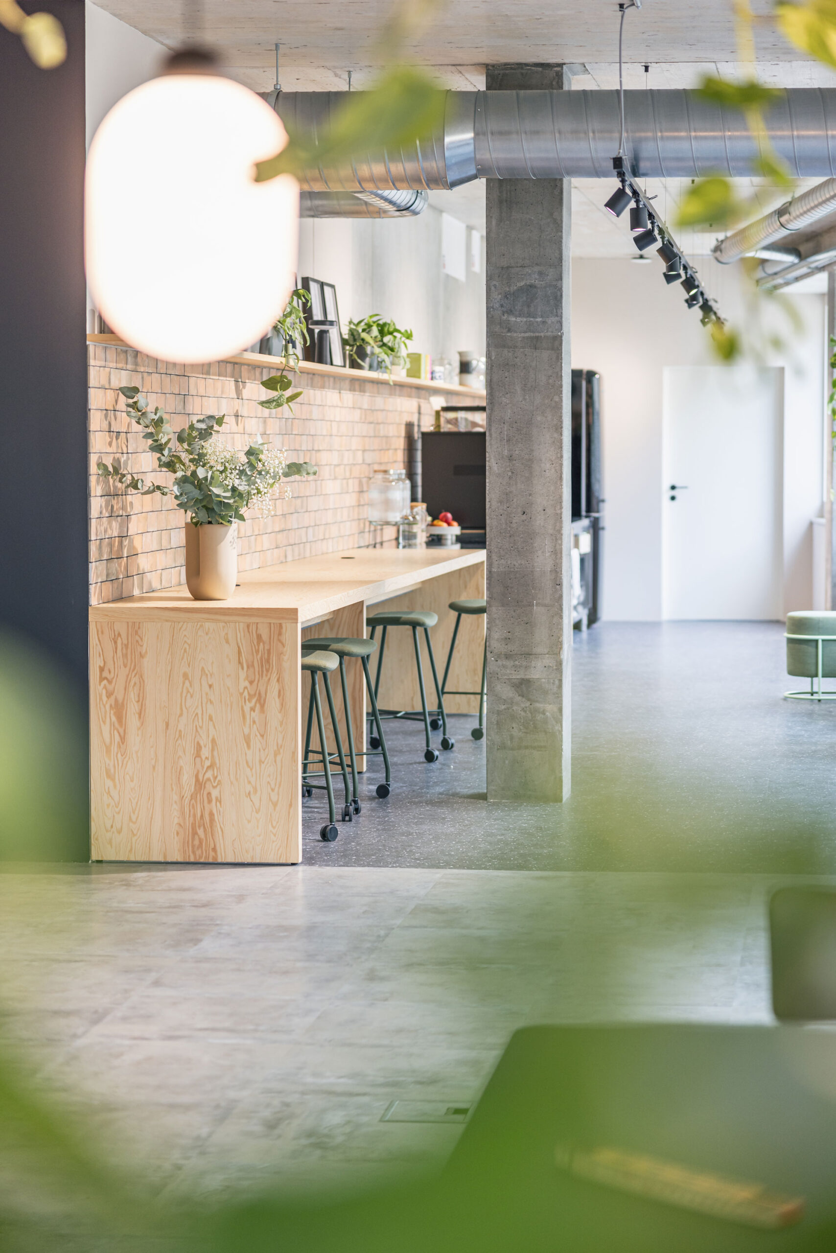 Stilvoller Bürobereich mit hoher Bartheke, Backsteinwand, Pflanzen und industriellen Designelementen.