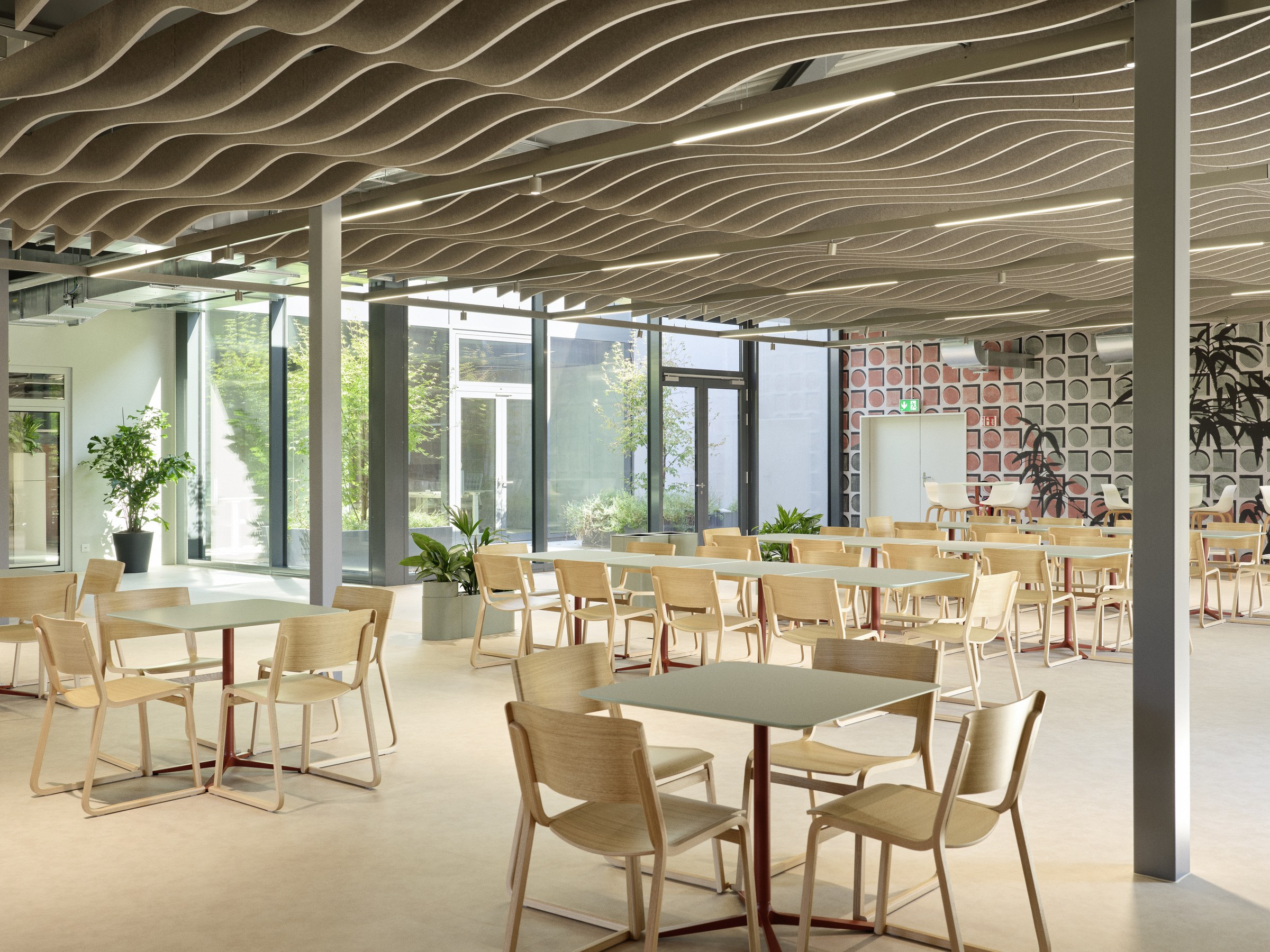 Cafeteria mit Bestuhlung und grünen Tischen.